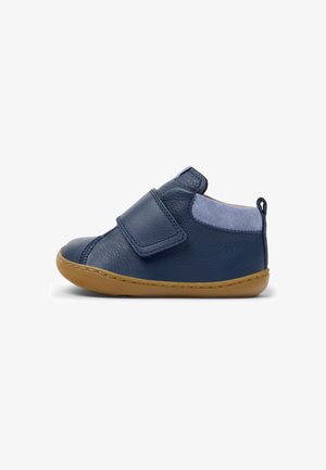 Blaues Lederschuh mit einem Klettverschluss, hellblauen Wildleder-Akzenten, abgerundeter Spitze und einer hellbraunen Gummisohle. Verfügt über eine hintere Schlaufe für ein einfaches Anziehen.