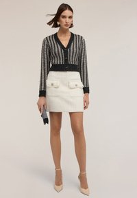 Cárdigan de punto a rayas en blanco y negro con botones, combinado con una minifalda de tweed color crema que cuenta con dos bolsillos frontales y detalles texturizados.