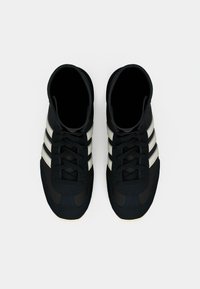 Un par de zapatillas negras de caña alta con rayas blancas y cordones negros, vistas desde arriba sobre un fondo blanco.