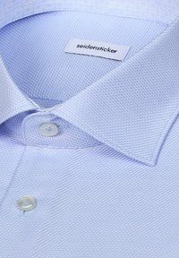 Chemise habillée bleu clair texturée avec des boutons blancs et une étiquette de la marque Seidensticker à l'intérieur du col.