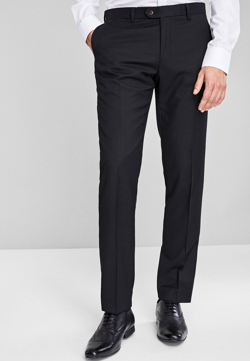 Pantaloni neri eleganti con taglio dritto, caratterizzati da una parte anteriore piatta, passanti per cintura e tasche. Indossati con scarpe eleganti in pelle nera.