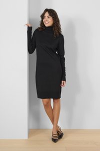 Black turtleneck dress with long sleeves, ribbed texture at collar and hem, mid-thigh length, paired with black strappy heels.