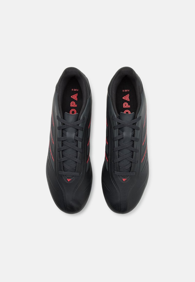 Zapatillas deportivas negras con una textura lisa, que presentan acentos y cordones rojos, un diseño de punta redondeada y detalles de costura lateral en un estilo moderno.