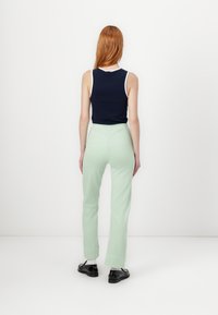 Ναυτικό αμάνικο τοπ με λευκή περιφέρεια, συνδυασμένο με ανοιχτό πράσινο παντελόνι σε χαλαρή γραμμή. Μαύρα παπούτσια ολοκληρώνουν την εμφάνιση.