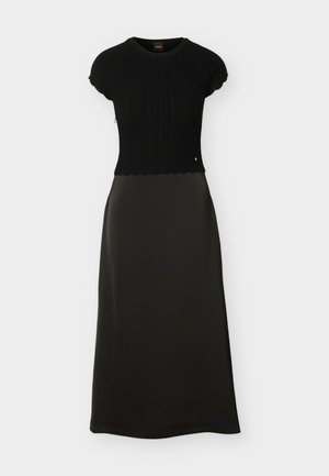 Melna midi kleita ar īsām piedurknēm, trikotāžas augšdaļa ar teksturētu rakstu un vilnainām malām, kopā ar gluda auduma A-līnijas svārkiem.