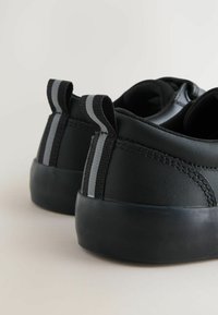 Czarne sneakersy o gładkiej skórzanej fakturze, z szarymi elastycznymi paskami na pięcie i czarną gumową podeszwą. Prosty, minimalistyczny design.