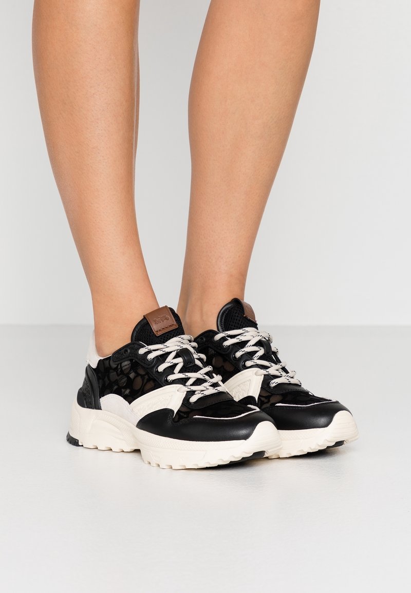 Černobílé tenisky s prodyšným svrškem, kontrastními koženými akcenty, kulatou špičkou, silnou podrážkou a béžovými detaily. Šňůrky jsou bílé.