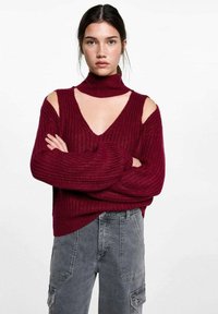 Bordový pletený sveter s otvoreným dizajnom na ramene, rolákom a hlbokým vykrojením do V. Nosí sa s šedými cargo nohavicami. Textúrovaná tkanina.