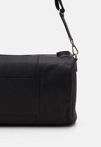 Svart läderhandväska med strukturerad yta, rektangulär form, dragkedjestängning ovanpå, justerbar rem och sidoficka.