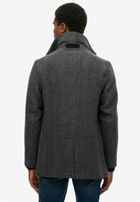 Abrigo de lana gris en patrón espiga con cuello caído, detalle de toggle en el cuello y un corte estructurado, combinado con unos jeans azul oscuro.