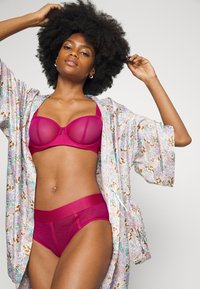 Sutiã magenta com painéis transparentes e uma peça alta combinando. Robe floral leve com cores pastel e um corte solto.