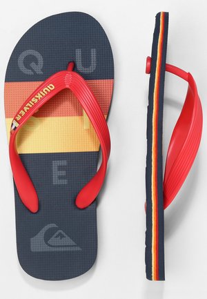 Par navyblå flip-flops med røde remme, gule og orange striber på fodsålen og stribet kant på sålen.