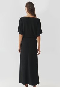 Schwarzes Strick-Maxikleid mit einem Bootsausschnitt und kurzen, breiten Ärmeln. Glatte Textur und voller Länge mit einem leichten Schwung am Saum.