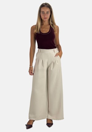 Beige weitgeschnittene Hose mit Falten, hoher Taille und Seitentaschen; kombiniert mit einem tiefburgunderfarbenen Tanktop. Glattes Material mit minimaler Textur.