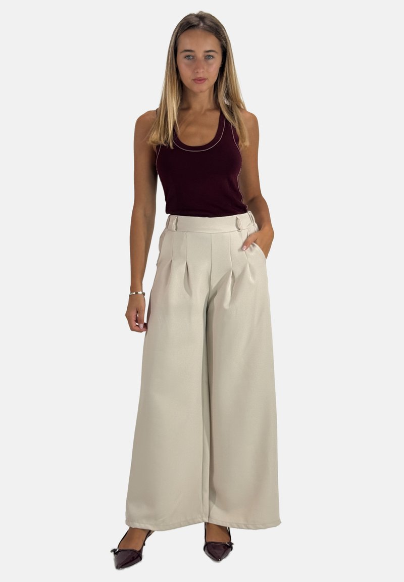 Beige wijde broek met plooien, hoge taille en zijzakken; gecombineerd met een diep bordeauxrood tanktop. Glad stof met minimale textuur.
