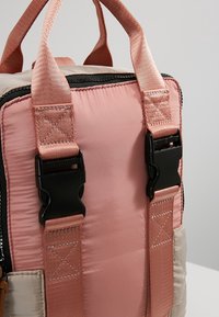 Ergonominen reppu, jossa on pehmeä vaaleanpunainen nylonpinta, tekstuurilla varustetut hihnat ja mustat muoviset kiinnityksentekijät turvallista kiinnittämistä varten.