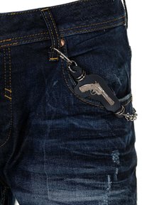 Denim-Jeans in dunkelblauer Farbe, mit auffälligen gelben Nähten und einem dekorativen Metallschlüsselanhänger in Form eines Revolvers.