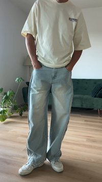 Camiseta oversize color beige claro, jeans de pierna recta en denim azul y zapatillas blancas con acentos grises. Ajuste casual con bolsillos frontales.