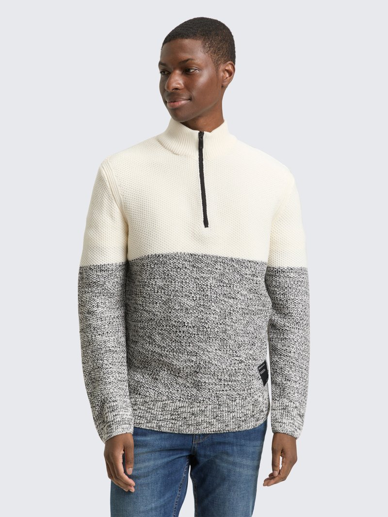 Sweater featuring a high collar, textured knit in cream and gray, with a black zip closure, and contrasting horizontal pattern.