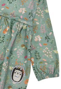 Grüner Stoff mit mehrfarbigen Blumen- und Tiermustern. Mit elastischen Bündchen und einem dekorativen Igel-Patch auf der Vorderseite.