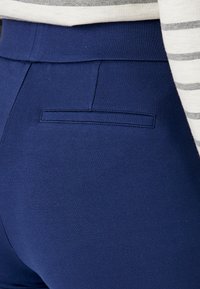 Marineblauwe broek van rekbare stof met een onopvallende achterzak en een gladde textuur. De tailleband heeft een schone, naadloze afwerking.