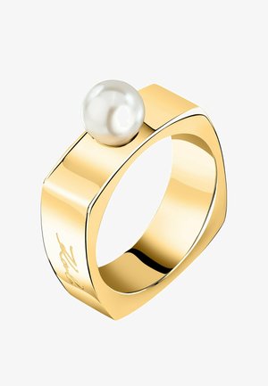 Bague de couleur dorée avec une finition lisse et polie. Elle présente une perle blanche proéminente sur le dessus, avec un design géométrique et des détails gravés.