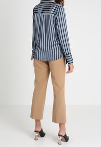 Blusa a righe blu e nera con maniche lunghe, pattina posteriore, abbinata a pantaloni cropped beige e tacchi neri con accenti metallici.