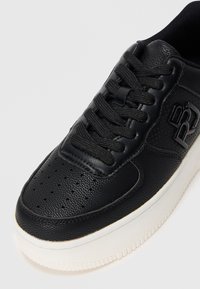 Baskets en cuir noir avec lacets noirs, bout perforé, panneau latéral texturé, détail de marque et semelle blanche épaisse.