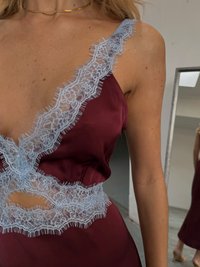 Burgundy satin dress with a deep neckline, featuring light blue lace trim and an open cutout at the waist, smooth texture, and delicate accents.