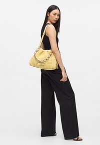 Sac à main matelassé jaune avec anse chaîne, doté d'une fermeture à cordon, d'un motif texturé et d'accents noirs contrastants.