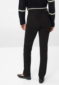 Jeans noirs à jambe droite avec une taille mi-haute, poches arrière et détails de couture subtils, associés à des ballerines noires.