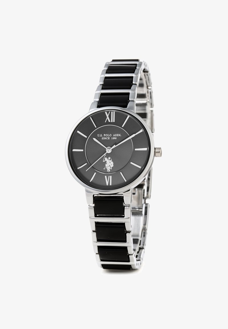 Montre argent et noire avec un cadran rond, des chiffres romains et un logo. Dispose d'un bracelet en acier inoxydable et émail noir pour un design élégant.