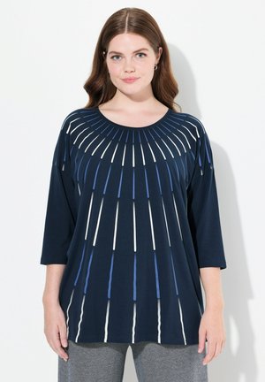 Maglietta blu navy con scollo rotondo, caratterizzata da accenti verticali a righe bianche e blu che si irradiano dal centro. Maniche a tre quarti.