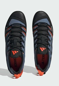 Niebieskie i czarne buty wspinaczkowe z pomarańczowymi akcentami, posiadające teksturowaną powierzchnię, wzmocniony gumowy czubek i solidny system sznurowania.