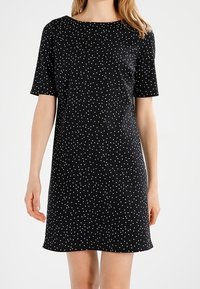 Černé šaty s krátkým rukávem, s kulatým výstřihem a bílými puntíky. Vyrobeno z hladké tkaniny s volným střihem, s délkou ke kolenům.