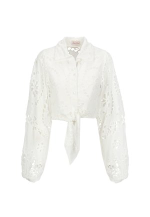 Camicia bianca cropped con maniche lunghe, caratterizzata da motivi floreali intagliati, chiusura con lacci frontale e colletto a punta. Tessuto morbido e leggero.