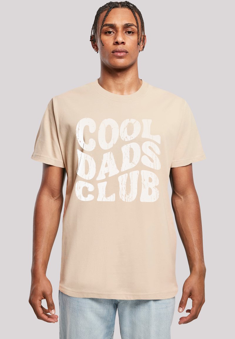Camiseta de algodón beige con gran texto blanco desgastado "CLUB DE PADRES GENIALES" en la parte frontal. Mangas cortas y cuello redondo.