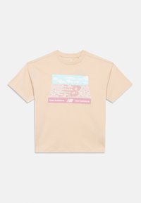 Camiseta beige de New Balance con un gráfico colorido de una multitud en un estadio bajo un cielo azul, con el logo de New Balance y texto.