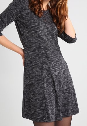 Robe en tricot noir et gris marbré avec une jupe évasée, des manches trois-quarts et un subtil détail de bouton au niveau du col.