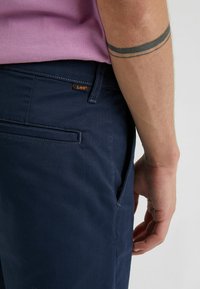 Pantaloni di cotone navy con una texture liscia, dotati di una tasca laterale e di un piccolo logo arancione Lee sulla vita.