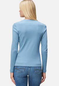 Chemise à manches longues bleu clair, fabriquée à partir d'un matériau doux, dotée d'un col rond et d'un design ajusté. Vue de dos, portée avec un jean bleu.