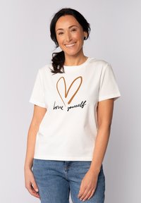 Witte katoenen t-shirt met korte mouwen, voorzien van een bruine hartomtrek en de tekst "hou van jezelf" in zwarte cursieve letters.