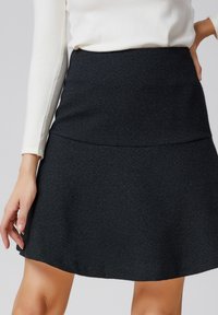Jupe tricotée noire avec une texture lisse, forme évasée et large ceinture. Longueur genoux, design sans couture sans embellissements.