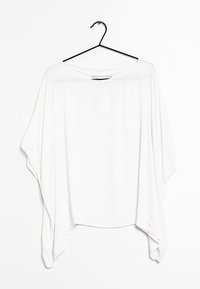 Blusa bianca sovradimensionata realizzata in un tessuto leggero. Presenta una scollatura ampia, spalle scese e un orlo asimmetrico. Appesa a un gancio nero.