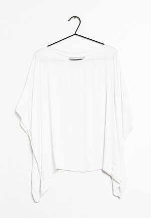 Blusa bianca sovradimensionata realizzata in un tessuto leggero. Presenta una scollatura ampia, spalle scese e un orlo asimmetrico. Appesa a un gancio nero.