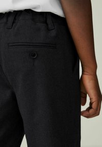 Schwarze Hosen aus strukturiertem Stoff verfügen über einen klassischen Knopfverschluss, eine Gesäßtasche mit Knopf und eine taillierte Passform.