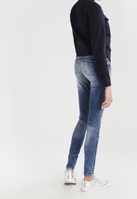 Slim jeans i blå denim, med en bleknad tvätt. Bärs med en marinblå jacka och silverfärgade sneakers, vilket framhäver en slimmad, åtsittande silhuett.