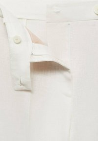 Witte linnen broek met een gedeeltelijke knoopsluiting, rits en verborgen zakdetails. Zachte textuur met strakke lijnen en eenvoudige stiksels.