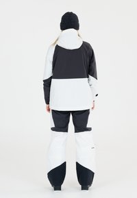 Sneeuwjack en broek in zwart en wit. Het jack heeft een capuchon, een kleurblokontwerp en elastische manchetten. De broek heeft verstelbare zoom.