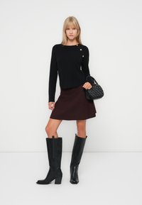 Un pull noir avec des boutons, une jupe bordeaux et des bottes en cuir noir jusqu'aux genoux. L'ensemble comprend un petit sac à main noir avec un design texturé.